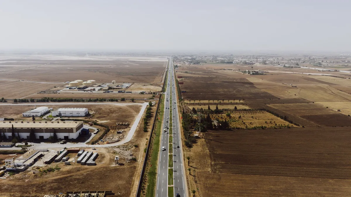 Carretera con bodegas industriales de un lado y campo de cultivo del otro